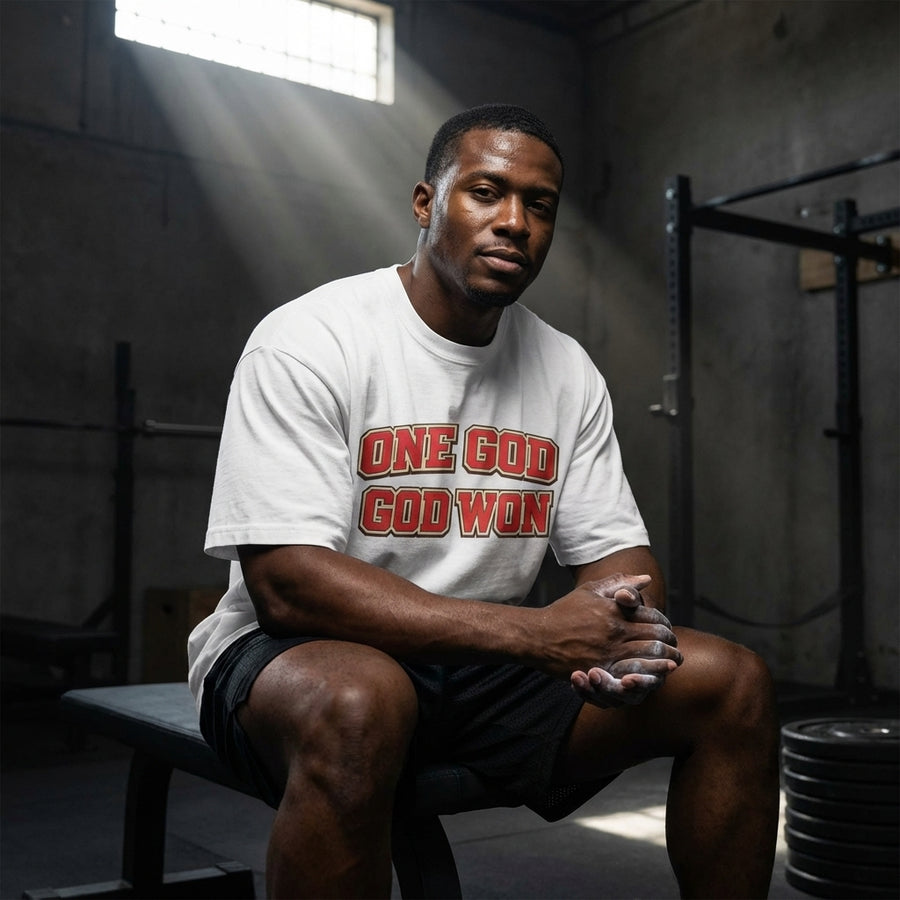 Man sitting on a bench in a gym wearing a white t-shirt with red text.