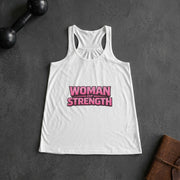 White tank top with 'Woman of Strength' text on a dark surface with dumbbells and a leather bag.